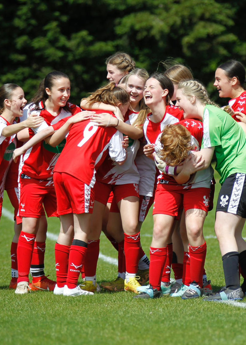 Group of female soccer players in red uniforms celebrating on a field.