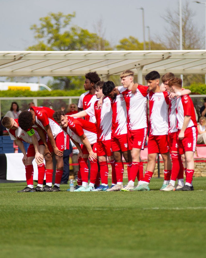 Football team in red and white uniforms standing on a field with spectators in the background.