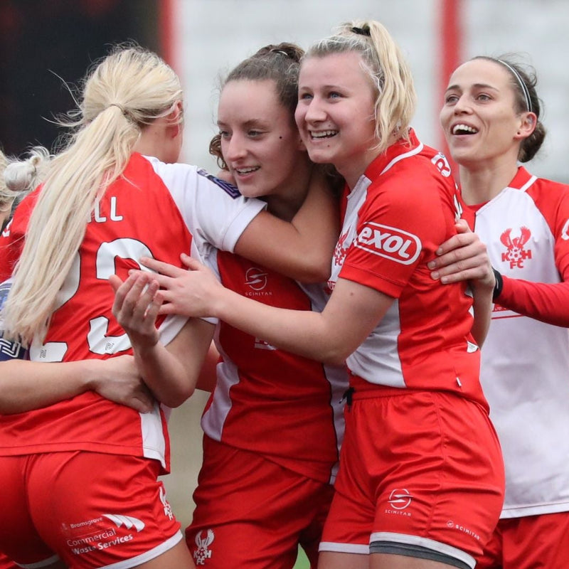 Group of female football players in red and white uniforms celebrating on a field.