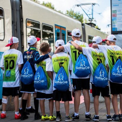 Group of children in sports attire with Gothenburg Cup bags standing near a tram.